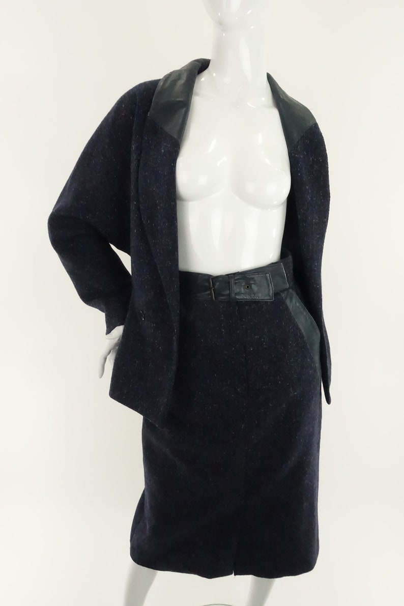 May include: A navy blue skirt suit with a black leather trim on the collar and pockets. The skirt has a black leather belt.