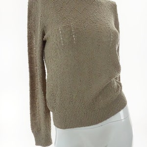 May include: A beige knitted sweater with a delicate openwork pattern. The sweater has long sleeves and a round neckline.