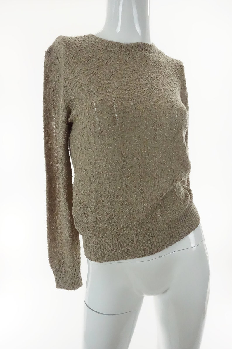 May include: A beige knitted sweater with a delicate openwork pattern. The sweater has long sleeves and a round neckline.