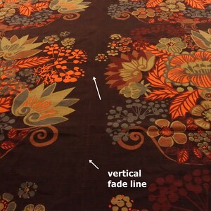May include: Close-up of a brown fabric with a repeating pattern of orange, red, and green floral designs. A vertical fade line is visible in the center of the image.