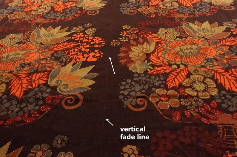 May include: Close-up of a brown fabric with a repeating pattern of orange, red, and green floral designs. A vertical fade line is visible in the center of the image.