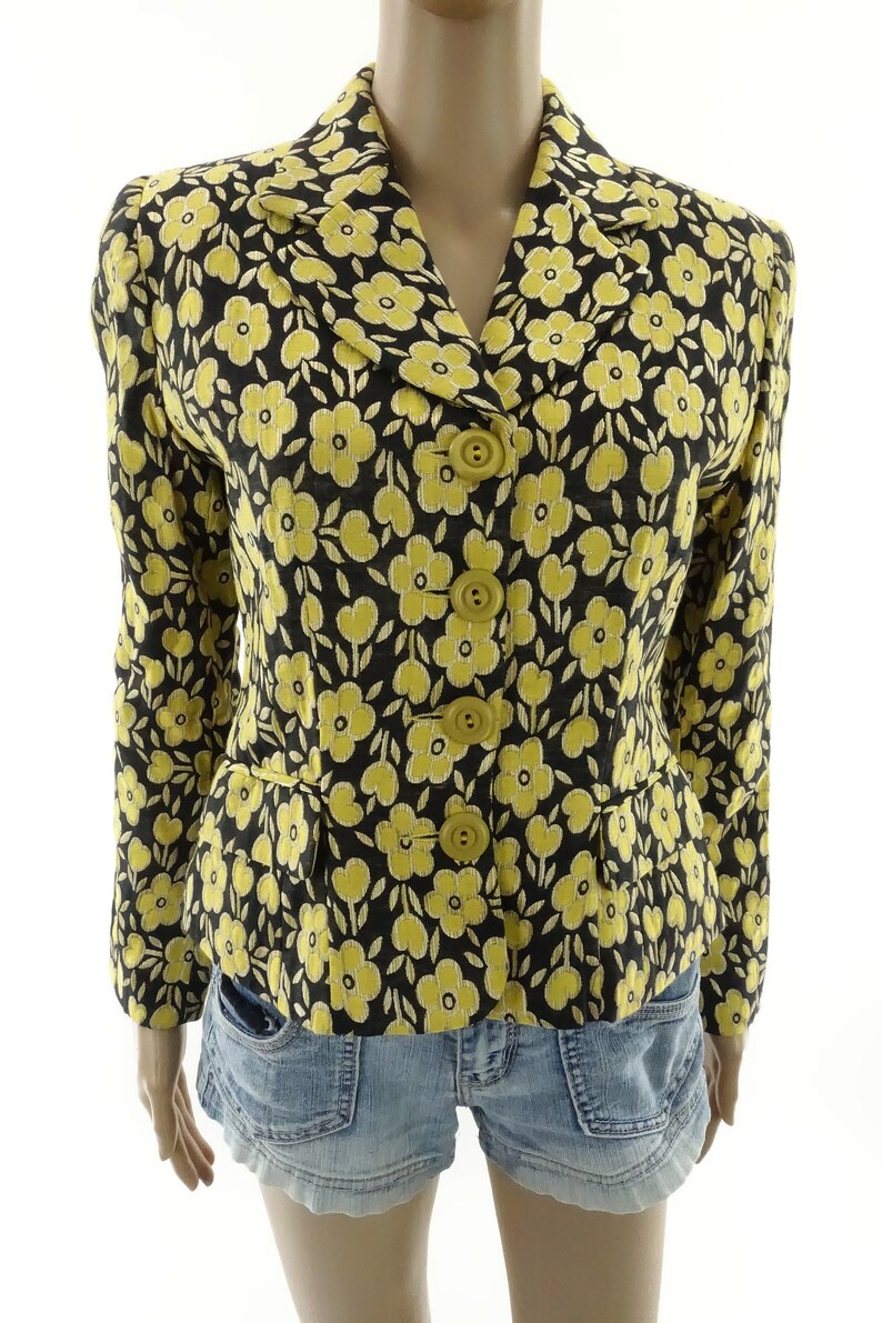Puede incluir: Una chaqueta negra con estampado floral amarillo con cierre de botones. La chaqueta tiene una silueta ajustada y est&aacute; hecha de una tela ligera.