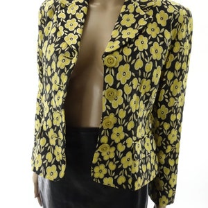 Puede incluir: Una chaqueta negra con estampado floral amarillo con cierre de botones. La chaqueta tiene una silueta ajustada y mangas largas.
