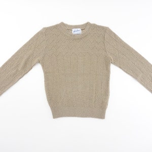 May include: A beige knitted sweater with a delicate openwork pattern. The sweater has long sleeves and a crew neckline.