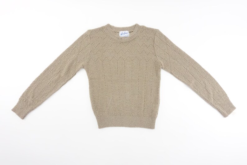 May include: A beige knitted sweater with a delicate openwork pattern. The sweater has long sleeves and a crew neckline.