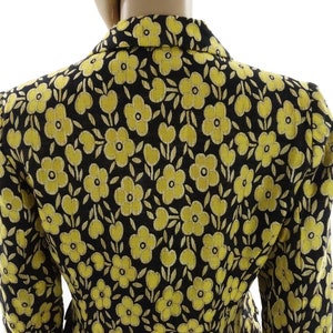 Puede incluir: Una chaqueta negra con estampado floral amarillo. La chaqueta tiene un corte cl&aacute;sico y un cuello.