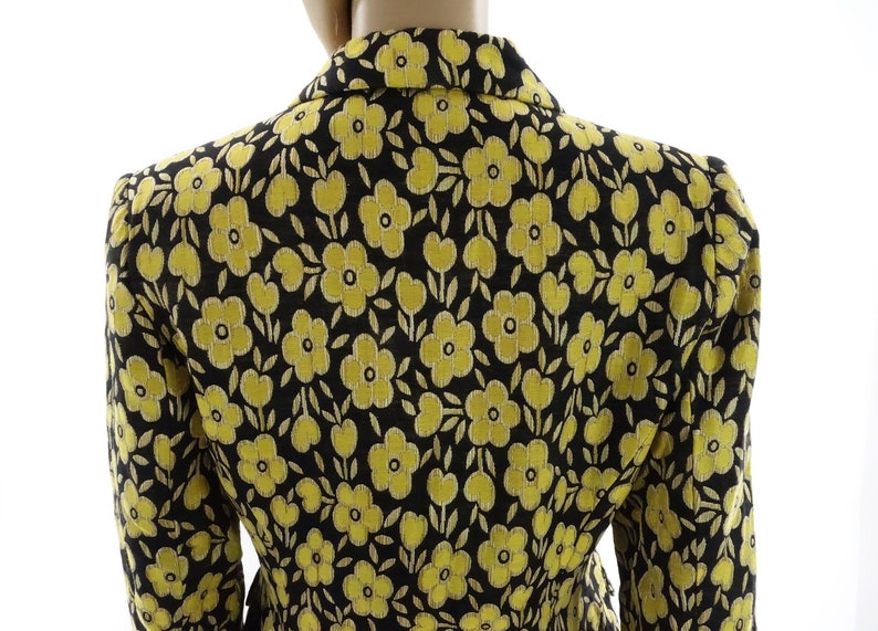 Puede incluir: Una chaqueta negra con estampado floral amarillo. La chaqueta tiene un corte cl&aacute;sico y un cuello.