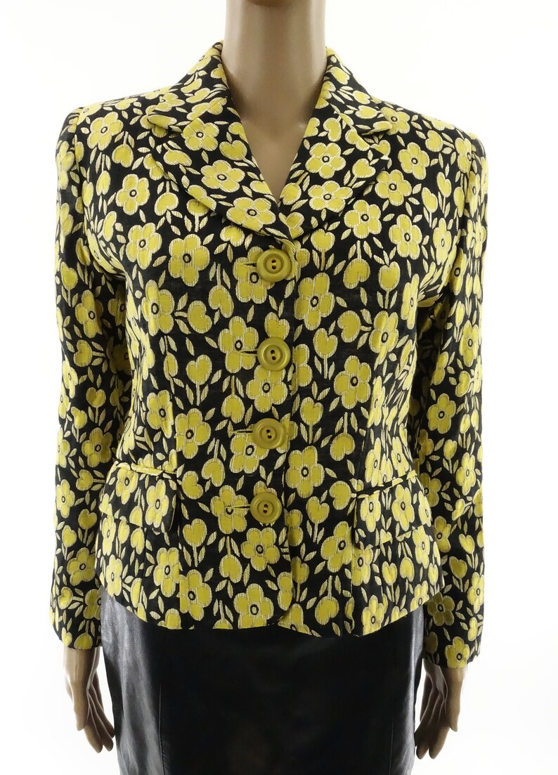 Puede incluir: Una chaqueta negra con estampado floral amarillo y cierre de botones.