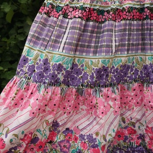 Op de afbeelding: Een gelaagde rok met een bloemenprint in tinten roze, paars en groen. De rok heeft een geruit patroon in het midden en een gerimpelde zoom.