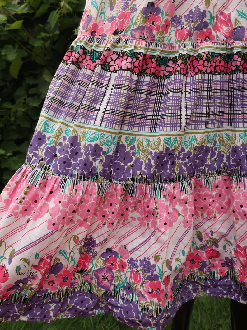 Op de afbeelding: Een gelaagde rok met een bloemenprint in tinten roze, paars en groen. De rok heeft een geruit patroon in het midden en een gerimpelde zoom.