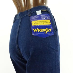 May include: Dark blue denim jeans with a Wrangler label attached to the back pocket. The label is blue and yellow and says "Boot cut, for her, jambe bottome, pour elle".