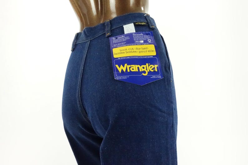 May include: Dark blue denim jeans with a Wrangler label attached to the back pocket. The label is blue and yellow and says "Boot cut, for her, jambe bottome, pour elle".