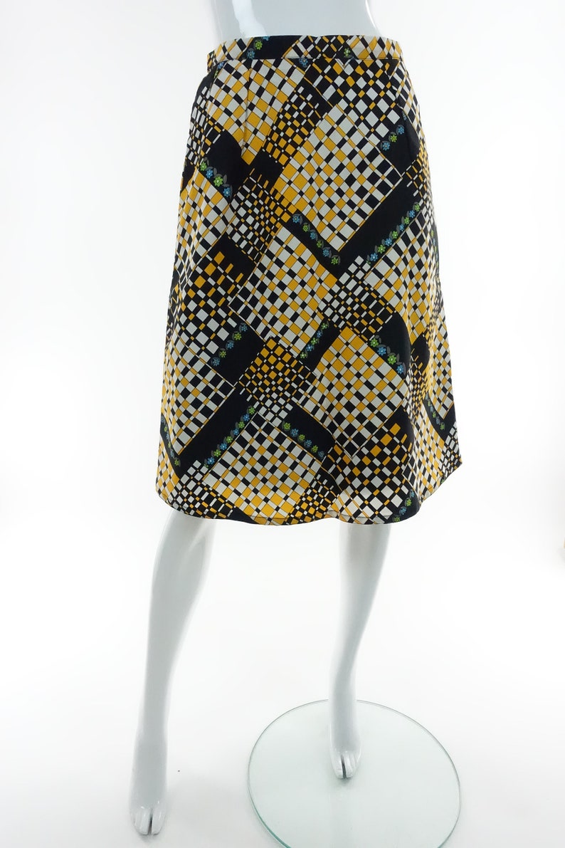 May include: A black, white, and yellow patterned skirt with a geometric design. The skirt is knee-length and has a straight silhouette.