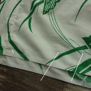 May include: Close-up of a white fabric with a green floral pattern. The fabric has a seam along the bottom edge.