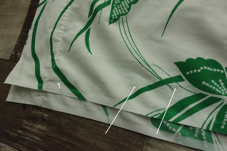 May include: Close-up of a white fabric with a green floral pattern. The fabric has a seam along the bottom edge.