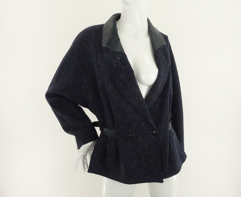 May include: A navy blue blazer with a black leather collar and a double-breasted closure. The blazer has a belt at the waist and a speckled pattern.
