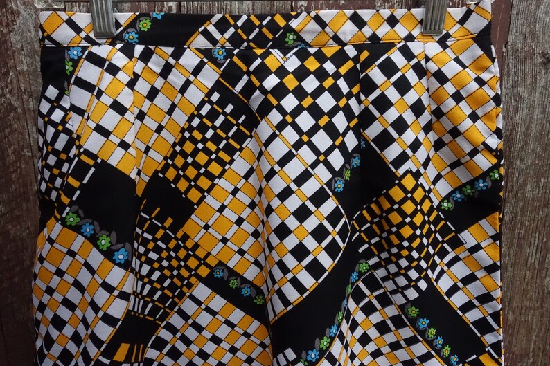 May include: A black, white, and yellow checkered skirt with a geometric pattern and small blue, green, and white flowers.