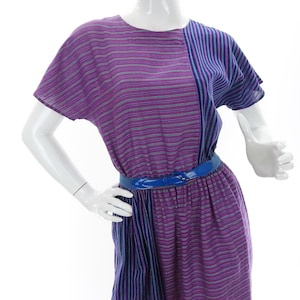 Peut inclure: Une robe à rayures violettes et bleues avec une ceinture en cuir verni bleu. La robe a des manches courtes et une coupe ample.