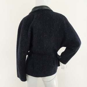 May include: A navy blue tweed jacket with a black leather collar and a black belt. The jacket has a slightly oversized fit and a relaxed silhouette.