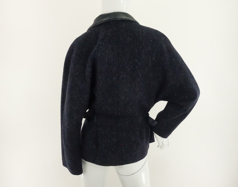 May include: A navy blue tweed jacket with a black leather collar and a black belt. The jacket has a slightly oversized fit and a relaxed silhouette.