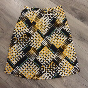 May include: A black, white, and yellow patterned skirt with a geometric design. The skirt is knee-length and has a flared silhouette.