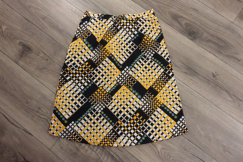 May include: A black, white, and yellow patterned skirt with a geometric design. The skirt is knee-length and has a flared silhouette.
