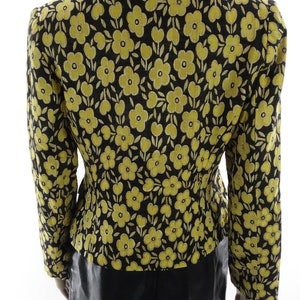 Puede incluir: Una chaqueta negra con estampado floral amarillo. La chaqueta tiene una silueta ajustada y mangas largas.