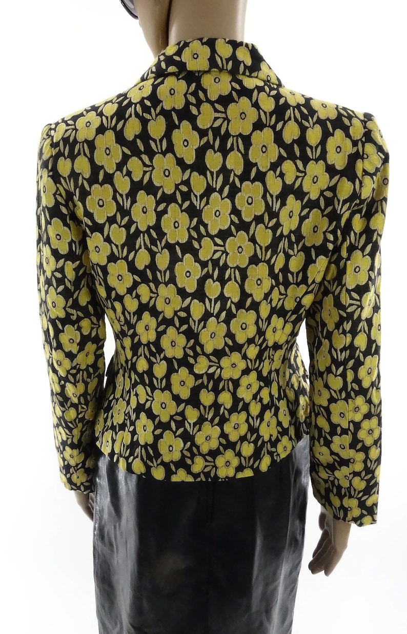 Puede incluir: Una chaqueta negra con estampado floral amarillo. La chaqueta tiene una silueta ajustada y mangas largas.