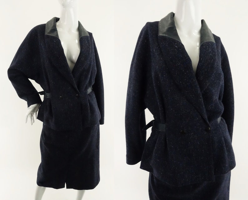 May include: A navy blue wool suit with a black leather collar and a double-breasted closure. The suit has a skirt and a jacket with a fitted waist.