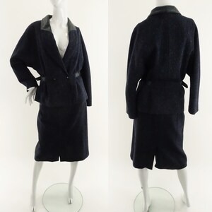May include: A navy blue skirt suit with a black leather collar and a matching belt. The suit is made of a textured fabric and has a fitted silhouette.