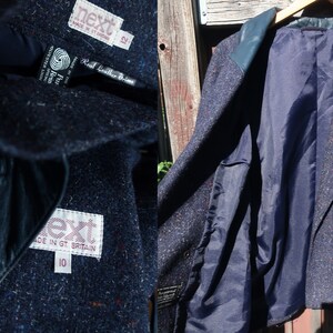 May include: A navy blue tweed blazer with leather trim. The blazer has a double breasted closure and a patch pocket on the left side. The inside of the blazer is lined with a navy blue fabric. The label on the blazer reads "Next" and "Real Leather Trims".