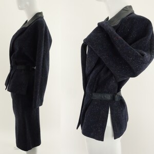 May include: A navy blue skirt suit with a black leather collar and belt. The jacket has a wrap-around style and a long sleeve.