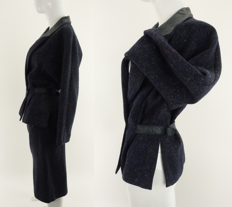 May include: A navy blue skirt suit with a black leather collar and belt. The jacket has a wrap-around style and a long sleeve.