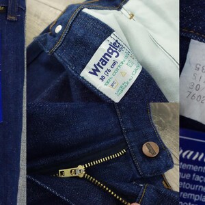 May include: A pair of dark blue denim jeans with a zipper fly and a Wrangler label. The label says "boot cut (for her) jambe bottee (pour elle)". The jeans have a size tag that says "S86 SIZE 30/34 7602P".