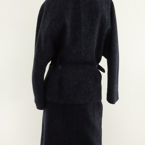 May include: A navy blue wool suit with a black leather collar and a matching belt. The jacket has long sleeves and a relaxed fit. The skirt is knee-length and has a straight silhouette.