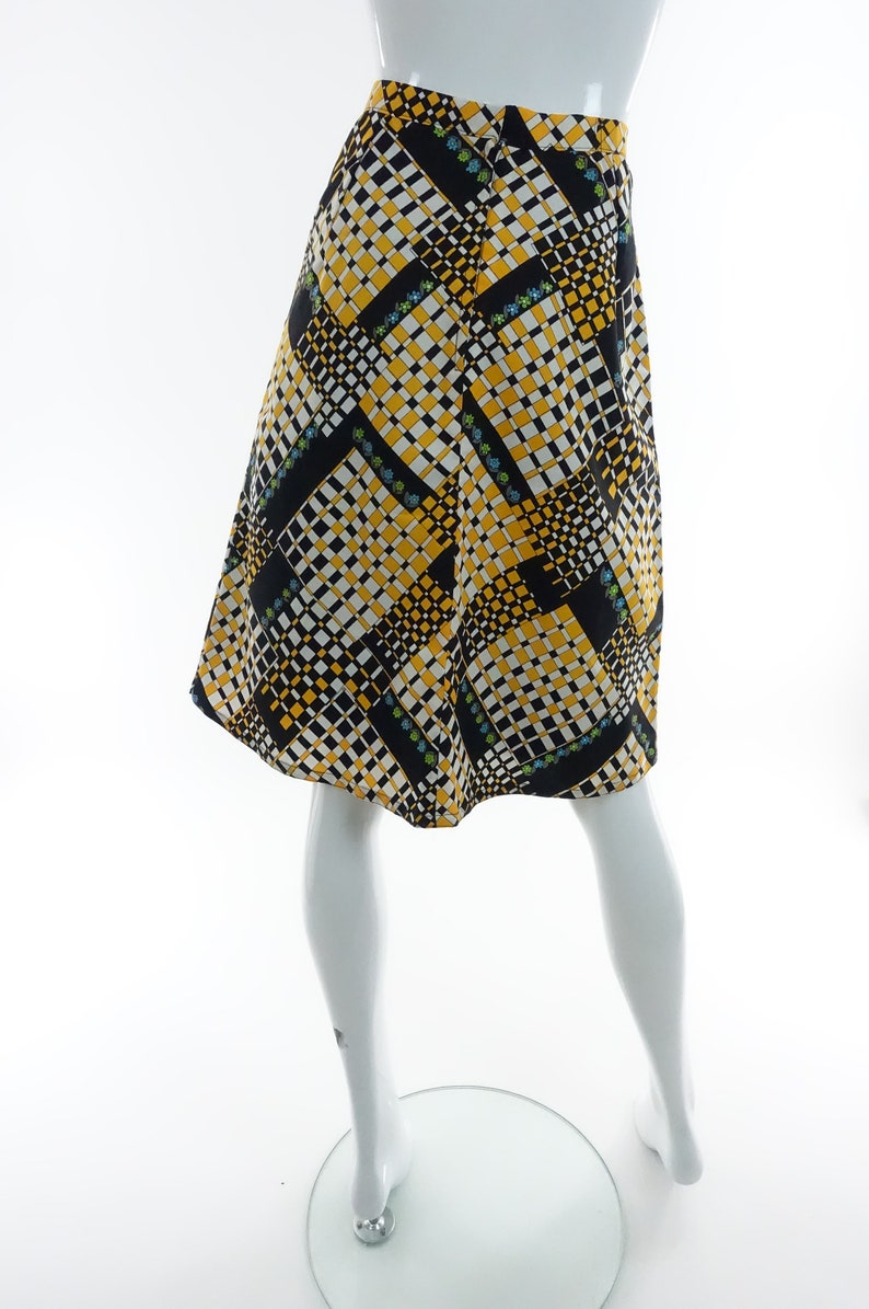 May include: A black, yellow, and white patterned skirt with a geometric design. The skirt is knee-length and has a fitted waist.