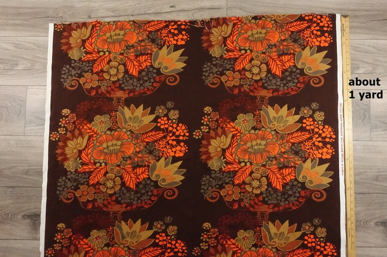 May include: A brown fabric with a repeating pattern of orange, yellow, and green floral bouquets. The fabric is about 1 yard long.