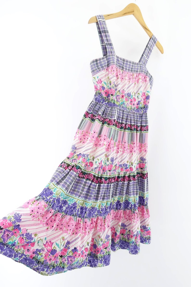 Op de afbeelding: Een gelaagde maxi-jurk met een bloemenprint in roze, paarse en groene tinten. De jurk heeft een vierkante halslijn en dunne bandjes.