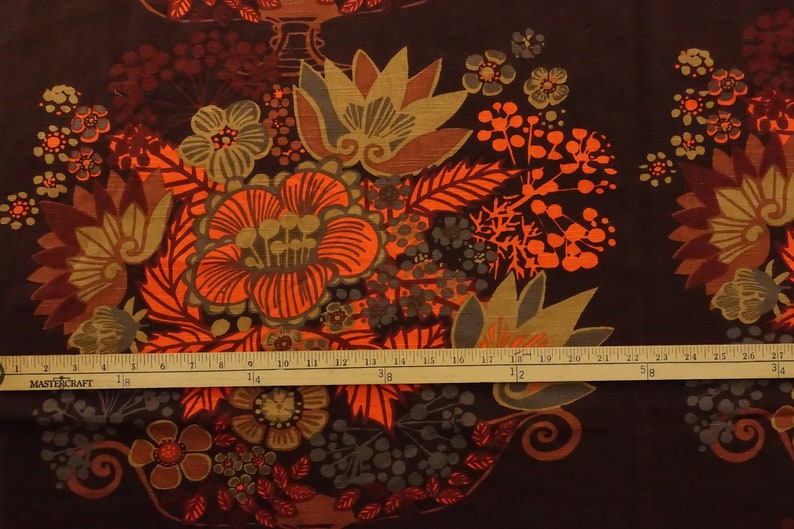 May include: A brown fabric with a repeating pattern of orange, brown, and green stylized flowers. The fabric has a vintage feel and would be great for upholstery or quilting.