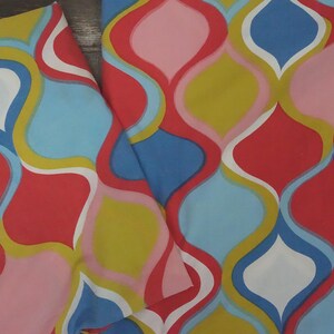 May include: A fabric featuring a repeating ogee pattern in vibrant shades of red, light blue, mustard yellow, pink, and white. The design consists of interlocking curved shapes that create a continuous, flowing geometric motif across the textile.