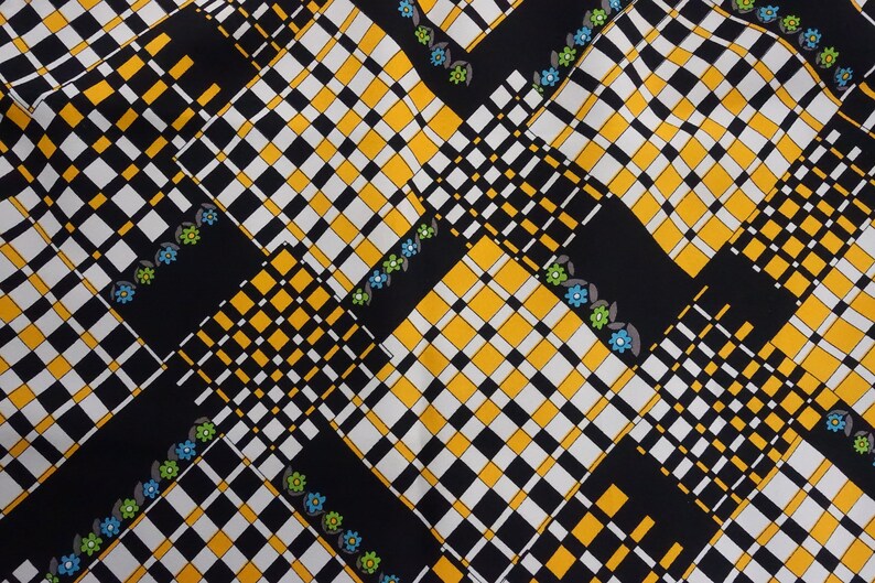 May include: Black fabric with a checkered pattern in white, yellow, and black. The fabric has a repeating pattern of small blue and green flowers.