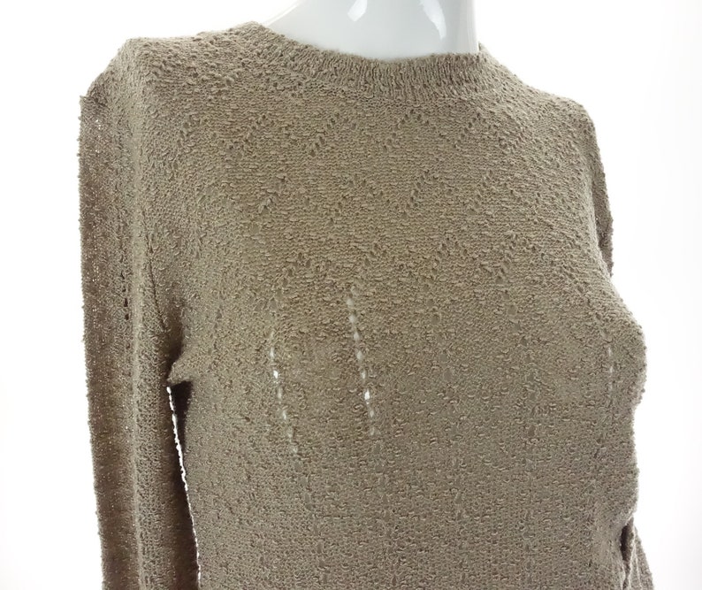 May include: A beige knitted sweater with a delicate openwork pattern. The sweater has long sleeves and a round neckline.