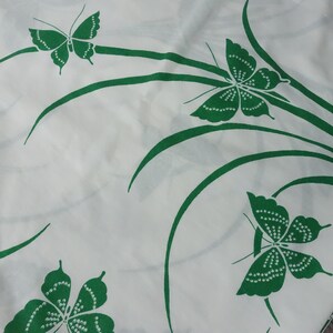 May include: White fabric with a green butterfly pattern. The butterflies are stylized and have a dotted design. The background is white and the butterflies are green.