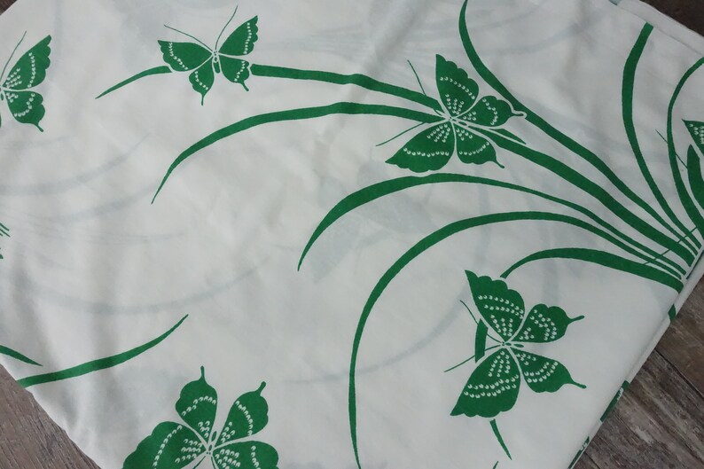 May include: White fabric with a green butterfly pattern. The butterflies are stylized and have a dotted design. The background is white and the butterflies are green.