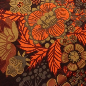 May include: A close-up of a fabric with a floral pattern. The fabric is brown, orange, and green. The flowers are stylized and have a retro look.