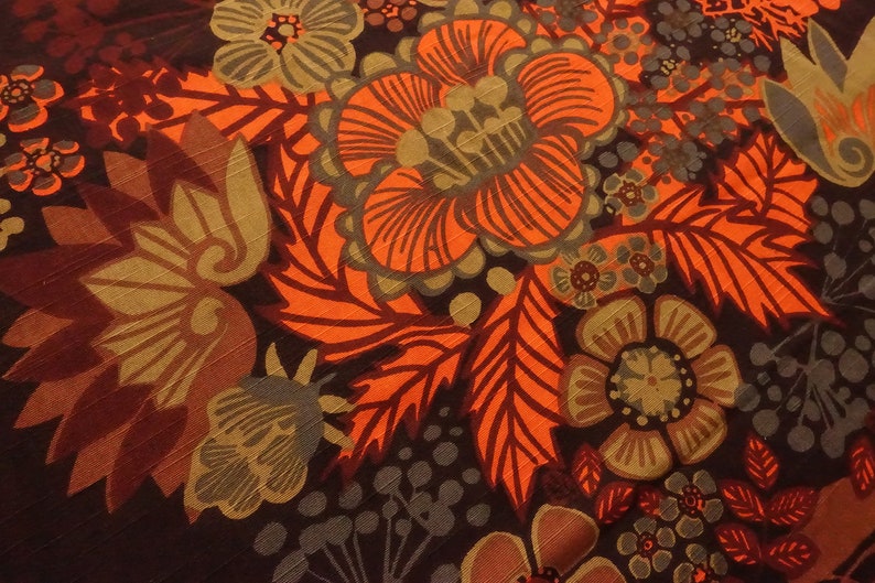 May include: A close-up of a fabric with a floral pattern. The fabric is brown, orange, and green. The flowers are stylized and have a retro look.