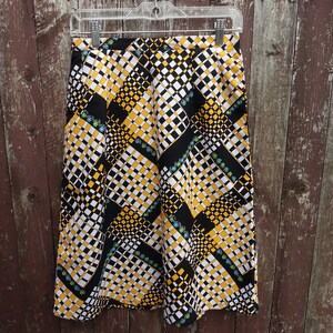 May include: A black, white, and yellow patterned skirt with a geometric design. The skirt has a high waist and a straight silhouette.