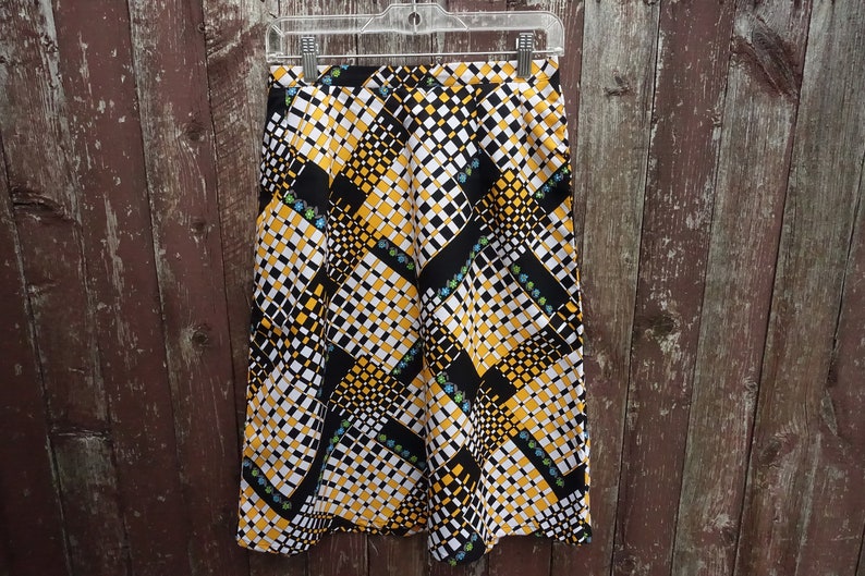 May include: A black, white, and yellow patterned skirt with a geometric design. The skirt has a high waist and a straight silhouette.