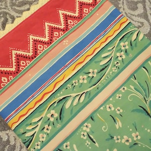 Peut inclure: Un tissu coloré avec un motif rouge en zigzag, des rayures roses, bleues et jaunes, et un motif floral vert. Le tissu a une bordure en dentelle jaune et est probablement utilisé pour la décoration intérieure ou l'artisanat.