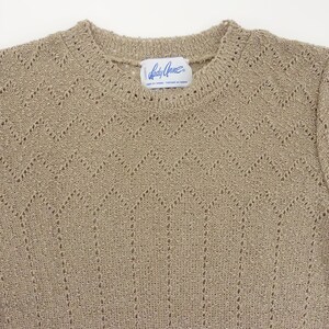 May include: A beige knitted sweater with a delicate openwork pattern. The sweater has a round neckline and long sleeves. The label reads "Lady Grace".